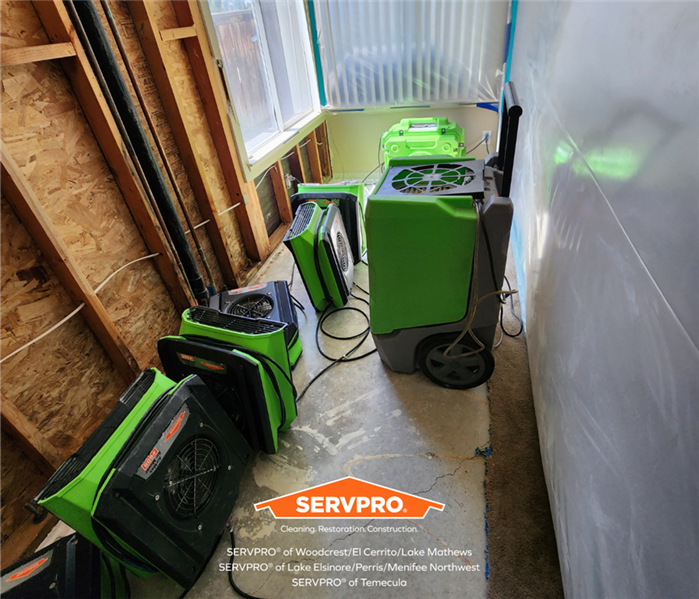 a water-damaged room with walls and insulation and carpet taken out and air movers and a dehumidifier